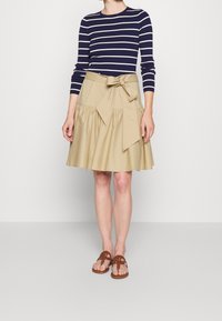 Gestreiftes navy und weißes Langarmshirt kombiniert mit einem beigen, taillierten, knielangen Rock mit gerafftem Design und gebundenem Schleifendetail.