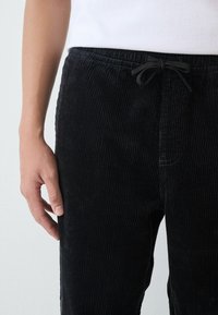 Black corduroy pants with a textured ribbed pattern, elastic waistband, and a drawstring closure. The fabric appears soft and durable.