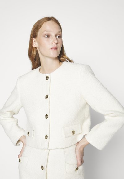 Λευκό σακάκι μπουκλέ με κομμένο σχέδιο, χρυσά κουμπιά και μπροστινές τσέπες. Το ύφασμα έχει μαλακή, υφασμάτινη εμφάνιση.
