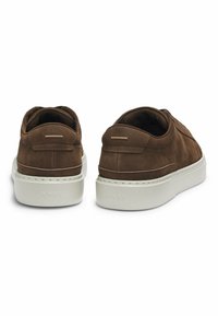 Braune Wildleder-Low-Top-Sneaker mit dicken weißen Gummisohlen, von hinten betrachtet, mit einem kleinen reflektierenden Streifen über der Ferse.