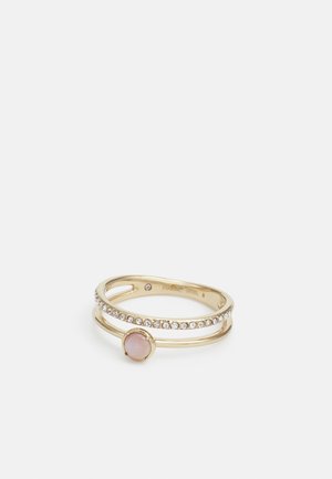 Bague double anneau en or avec de petites pierres claires sur un anneau et une pierre ronde rose pâle sur l'autre anneau, présentée sur fond blanc.
