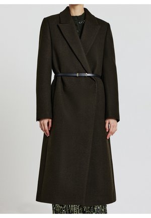 Manteau long en laine marron foncé avec ceinture et larges revers, porté sur une jupe à sequins, présenté sur une personne devant un fond clair uni.