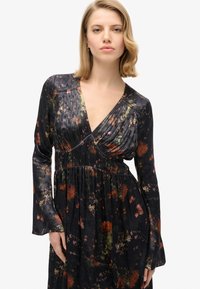 Vestido negro de manga larga con patrón floral, escote pronunciado, cuerpo plisado y falda fluida. Tejido suave con un acabado satinado.