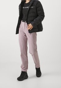 Black puffy jacket, fitted pink pants, black hiking boots. Fabrics appear smooth; jacket features a logo and zippers. Pants have a sleek design.