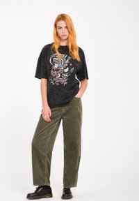 T-shirt nera oversize con stampa grafica, abbinata a pantaloni in velluto verde e scarpe nere. Semplice, vestibilità rilassata e tessuto testurizzato.