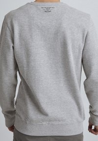 Sudadera gris con cuello redondo, puños y dobladillo acanalados. Presenta una etiqueta impresa en la parte posterior del cuello. Fabricada con una tela suave y lisa.