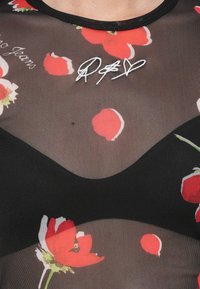 Black mesh top featuring red floral patterns. Round neckline, short sleeves, with handwritten white signature detail on the front.