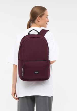 Bordeauxfarbener Rucksack mit glattem Stofffinish, ausgestattet mit einer vorderen Reißverschlusstasche, verstellbaren Trägern und einem oberen Tragegriff. Logo vorne angebracht.