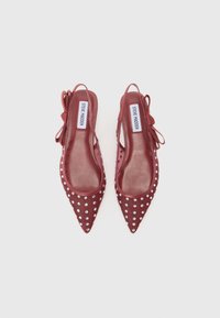 Sandales à talons en maille rouge avec bout pointu, embellies de clous en argent, dotées d'un détail de nœud sur le talon et d'un intérieur lisse.