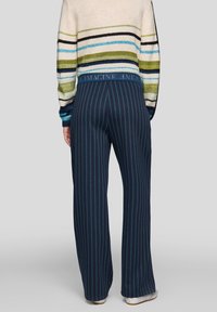 Marineblaue, weit geschnittene Hosen mit breiten Streifen, weicher Textur und elastischem Bund, mit einem hellblauen Akzentstreifen und dem Wort "IMAGINE" auf dem Bund.