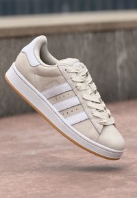 Beige semsket sneakers med hvit tre-stripes branding, snøring design og gummigummi såle. Har "CAMPUS" tekst på utsiden.