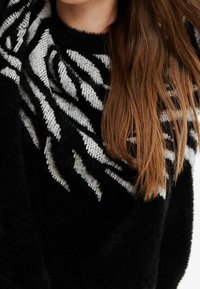 Schwarzer, fuzzie Pullover mit einem Zebra-Muster in weißem und grauem Strickmuster, mit rundem Ausschnitt und langen Ärmeln.