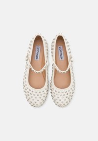 Scarpe Mary Jane bianche con punta arrotondata, decorate con borchie argentate, dotate di una fascia sulla parte superiore del piede e una finitura in pelle liscia.