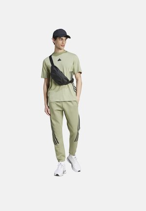 Men's athletic outfit featuring a light green T-shirt with black logo, matching joggers with black side stripes, and white sneakers.