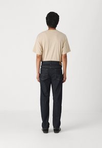 Camiseta de manga corta beige combinada con jeans de mezclilla azul oscuro. Los jeans cuentan con dos bolsillos traseros y una cinturilla visible con una etiqueta.