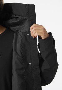 Czarna kurtka z gładkim zewnętrzem, wyposażona w podszyte wnętrze, zapięcia na zatrzaski oraz częściowo otwarty przód odsłaniający prostą czarną koszulkę pod spodem.