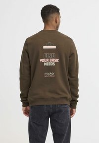 Sudadera marrón con cuello redondo, que presenta texto impreso en la parte posterior. La tela parece suave, con puños y dobladillo acanalados.