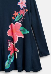 Laivastonsininen ribbineulottu mekko, jossa on eläväiset kukkakuvioinnit vaaleanpunaisessa, korallin sävyissä ja vihreässä. Hieman levenevä helma ja pitkät hihat pyöreillä kalvosimilla.