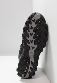 Schwarzer Wanderschuh mit einer strukturierten Gummisohle und auffälligen Profilen, grauen Akzenten und einer atmungsaktiven Mesh-Oberfläche. Geeignet für Outdoor-Aktivitäten.