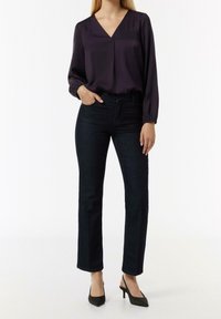 Blouse violette foncée à col en V avec manches longues, associée à un jean droit bleu foncé en denim et des talons noirs pointus. Tissu lisse et lignes épurées.