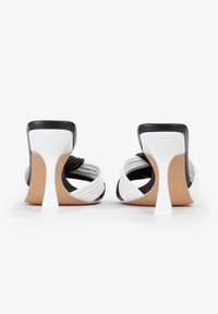 Scarpe con tacco alto e cinturini con una combinazione di colori bianco e nero. Presentano un design elegante, una texture a coste e un tacco a stiletto.