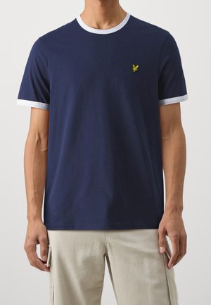 Mann trägt ein marineblaues T-Shirt mit weißen Abschlüssen an Ärmeln und Kragen, kombiniert mit hellbeigen Cargo-Hosen.