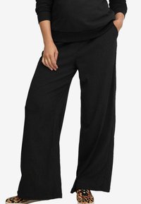 Zwarte wijde broek met een gladde textuur, elastische taille en zijzakken, gecombineerd met schoenen met dierenprint.