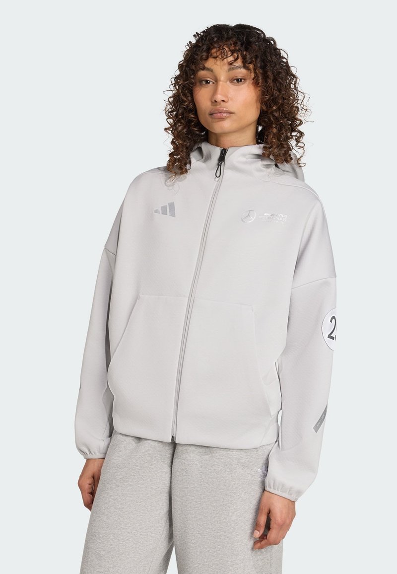 Hellgrauer Reißverschluss-Hoodie aus strukturiertem Stoff, mit Fronttaschen, Kapuze und Mercedes- sowie Adidas-Logos auf der Brust und dem Ärmel.