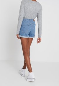 Grå långärmad tröja, blå denimshorts med uppvikta ben, och vita högskaftade sneakers, sedd från baksidan.