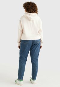 Hoodie rosa corto con cappuccio, abbinato a jeans blu a vita alta e sneakers con dettagli verdi. Tessuto morbido, vestibilità casual.