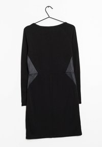 Robe noire à manches longues avec une coupe ajustée, présentant des panneaux en maille transparente sur les côtés et un décolleté arrondi. Suspendue à un crochet noir.