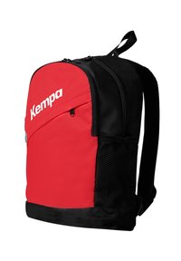 Rode en zwarte rugzak met een gestructureerde stof, een ritsvak aan de voorkant, een mesh zijvak en een wit "Kempa" logo aan de voorkant.