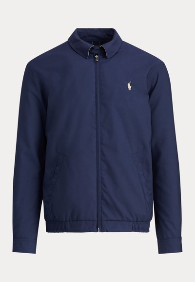 Marineblaue Jacke mit Reißverschluss, Stehkragen, elastischem Bund, Seitentaschen und kleinem weiß besticktem Polo-Spieler-Logo auf der Brust.