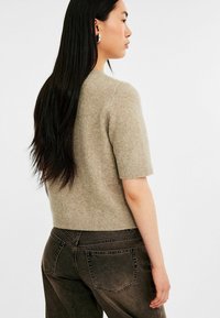 Beige gebreide trui met korte mouwen en een geribde halslijn, gecombineerd met hooggeknoopte donkerblauwe spijkerbroek met achterzakken en zichtbare stiksels.