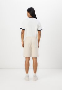 Hvid kortærmet t-shirt med marineblå detaljer, parret med beige shorts med elastisk talje og sidelomme. Båret med hvide sneakers.