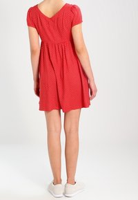 Röd klänning med korta puffärmar, V-ringning bak, rynkad midja och vita prickar. Bärs med vita sneakers.