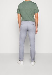 Šedé chino kalhoty s úzkým střihem, ohrnutými lemy, dvěma zadními kapsami a hladkým povrchem, doplněné zeleným pruhovaným tričkem.