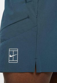 Nike shorts in dark blue fabric feature a white logo and grid detail. The design includes a side pocket and a slight split at the hem.