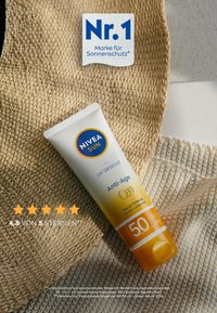 NIVEA SUN Anti-Age UV-Creme mit SPF 50, weißer Tube mit gelben Akzenten, verfügt über Q10-Beschriftung, strukturierter Hintergrund.