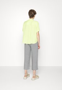 Camisa de manga curta verde claro, ajuste solto; calças largas cinzas com padrão; sandálias de plataforma bege com cintas verdes; vista traseira.