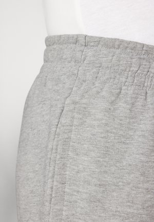 Close-up af grå joggingbukser med elastisk talje og sidelomme, båret med en hvid top.