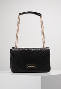 Czarna torba z pikowanej skóry z wzorem w zygzak, złotym łańcuchem oraz markową plakietką z przodu. Prostokątny kształt z wyraźnym designem.