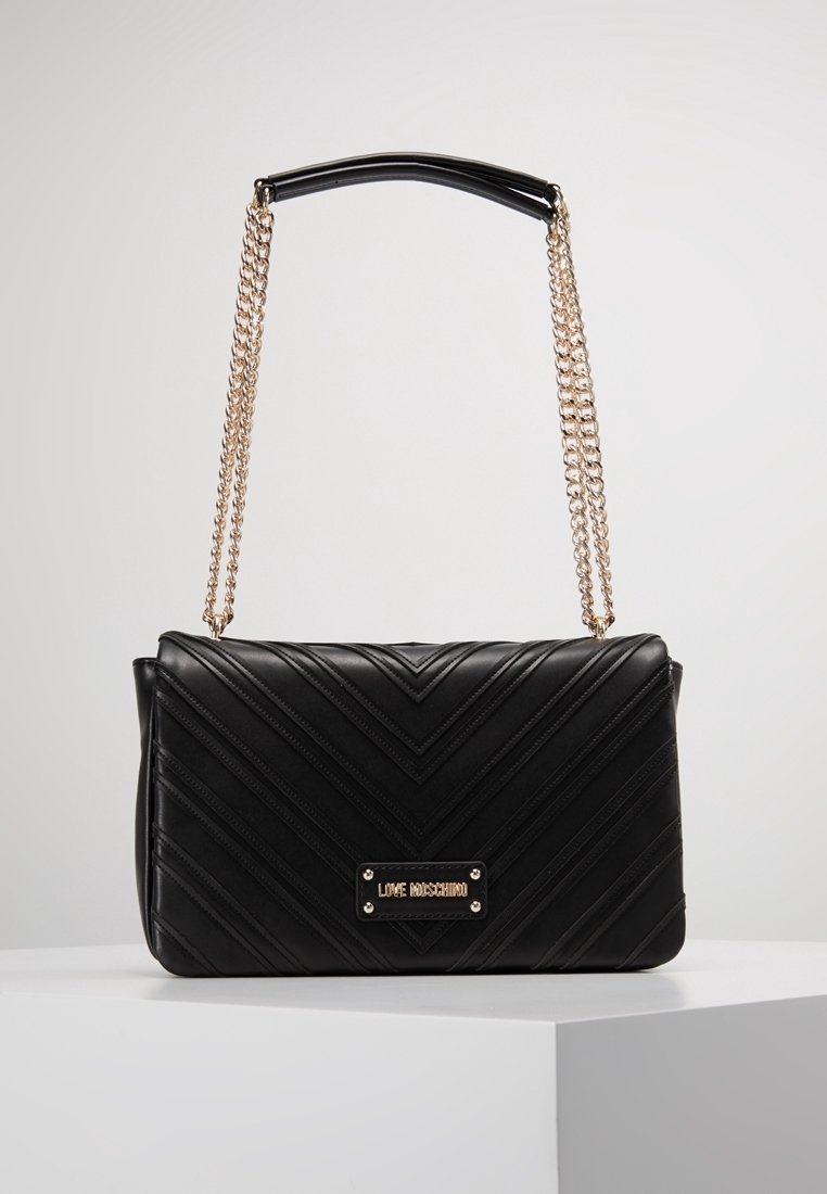 Czarna torba z pikowanej skóry z wzorem w zygzak, złotym łańcuchem oraz markową plakietką z przodu. Prostokątny kształt z wyraźnym designem.