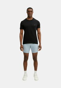 T-shirt nera a maniche corte con un logo discreto sul petto, abbinata a pantaloncini azzurri chiari e scarpe da ginnastica bianche. Abbigliamento sportivo semplice e moderno.