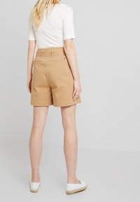 Beige katoenen shorts met een ontspannen pasvorm, voorzien van een tailleband met riemlussen en een model dat boven de knie valt, gecombineerd met witte espadrilles.