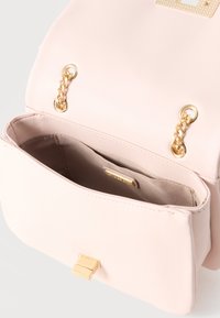 Bolso de mano de cuero rosa claro con detalles en cadena dorada, solapa abierta y bolsillo interior de tela beige.