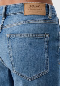 Os jeans de ganga azul-claro apresentam uma vista traseira com um rótulo de marca em couro, dois bolsos traseiros com um design de costura simples.