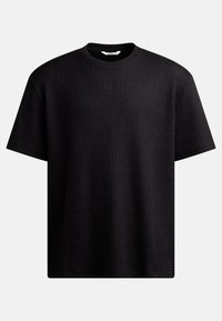 Svart T-skjorte med korte ermer som har et teksturert vaffelstrikket design og rund hals. Laget av mykt materiale, med en løs og avslappet passform.