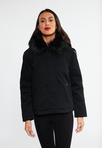 Sort, isoleret jakke med en tekstureret faux fur krave, lynlås-lomme på siden og en let boxy silhuet.