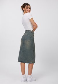 Jupe midi en denim bleu délavé, avec une taille haute, des poches arrière et une silhouette droite. Portée avec un t-shirt blanc ajusté et des baskets.